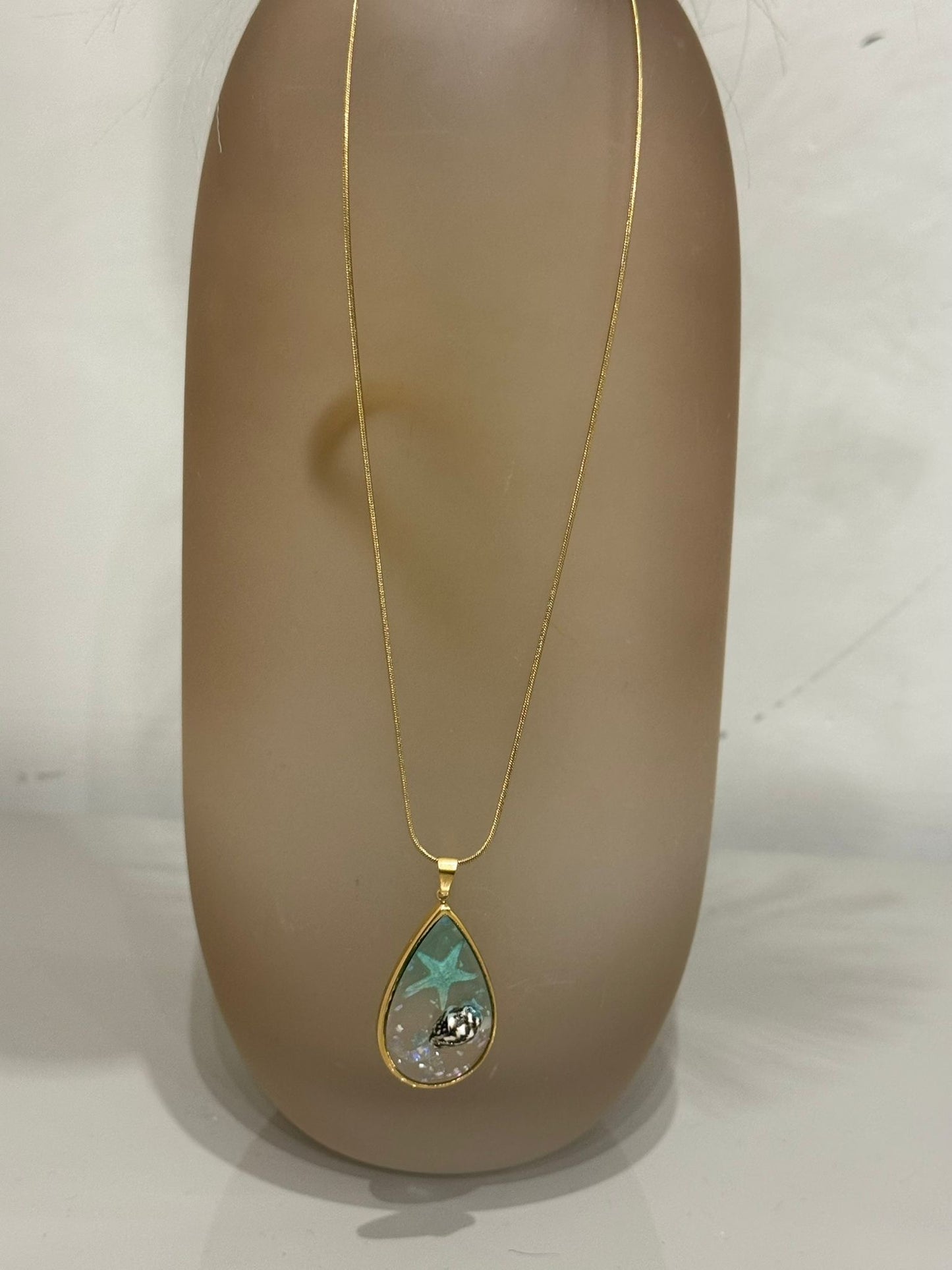 Collana Sharm base oro con ciondolo a goccia contenente una stella marina e una conchiglia incapsulata