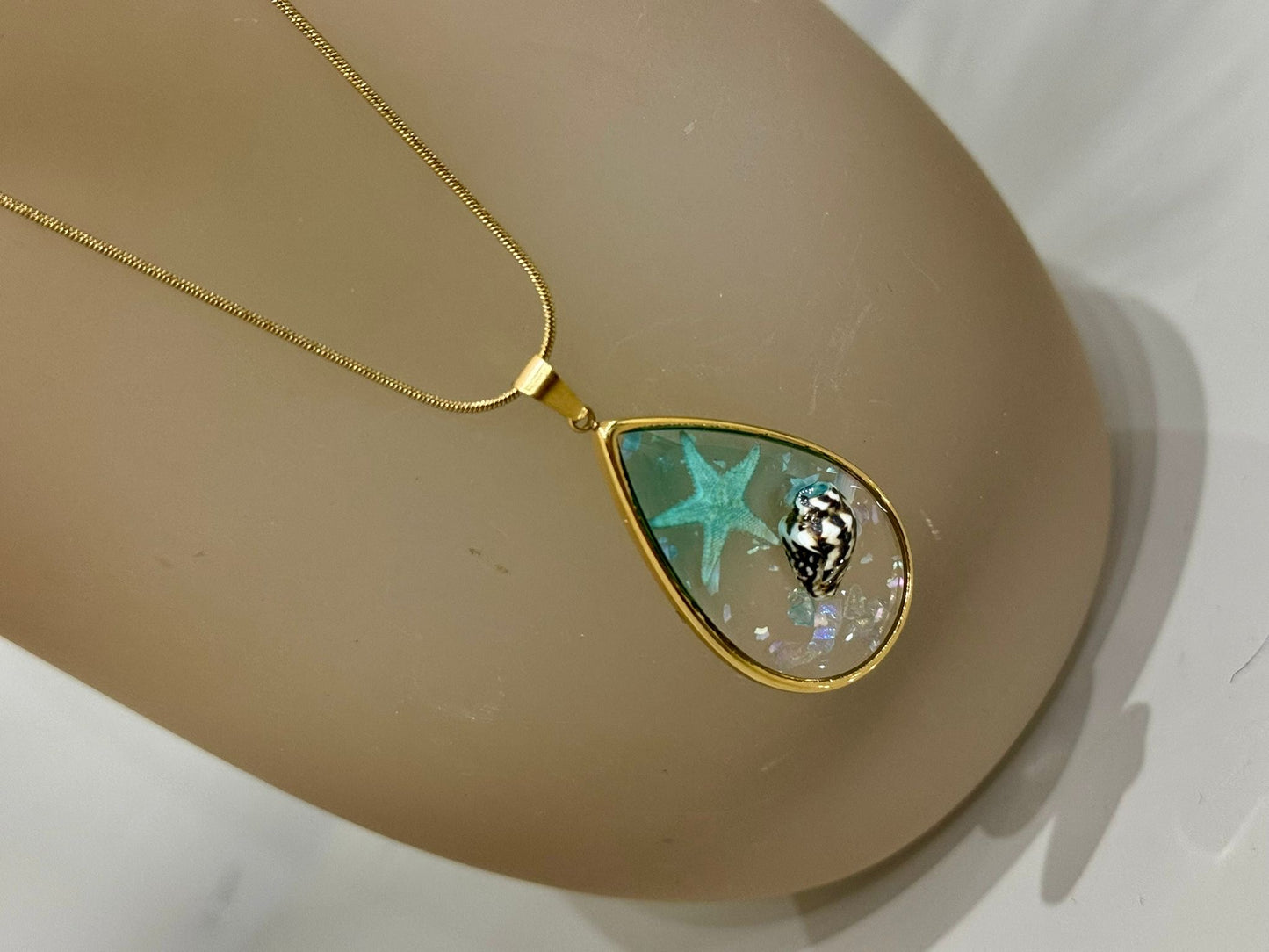 Collana Sharm base oro con ciondolo a goccia contenente una stella marina e una conchiglia incapsulata